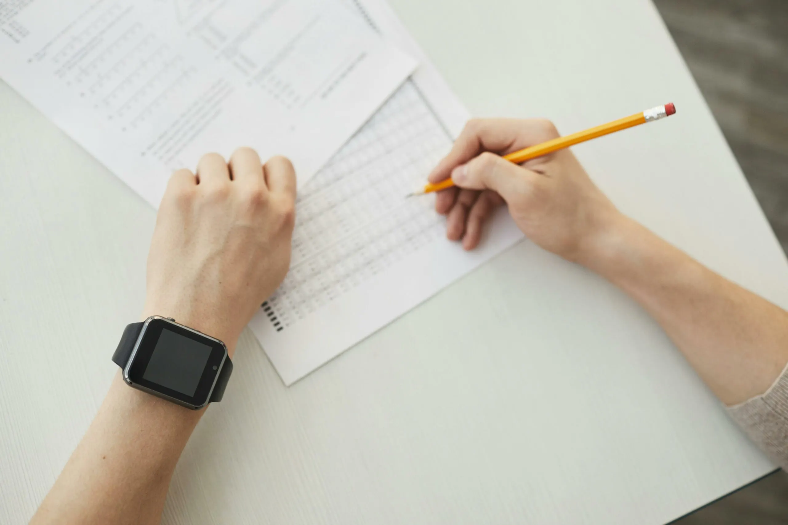 Nursing student using NCLEX test-taking strategies while writing on an exam answer sheet with a pencil