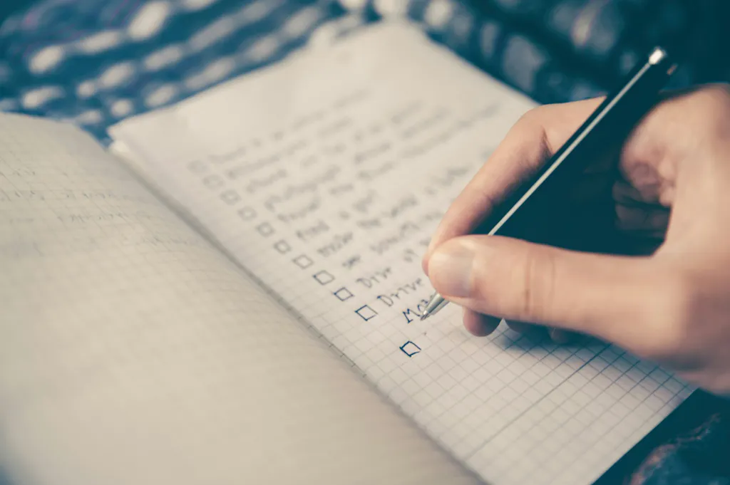 Hand checking off items on a handwritten list, representing how to work through the ANCC FNP Test Content Outline 2026 domain by domain