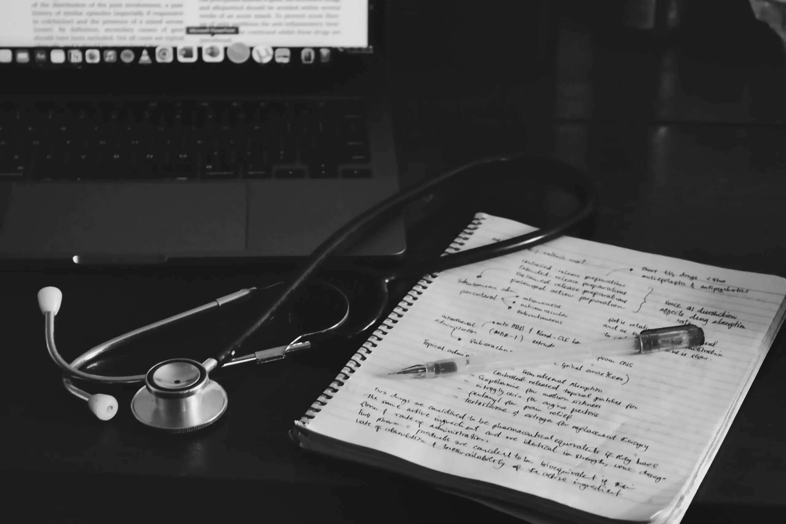 Handwritten pharmacology notes on drug administration routes beside a stethoscope and laptop