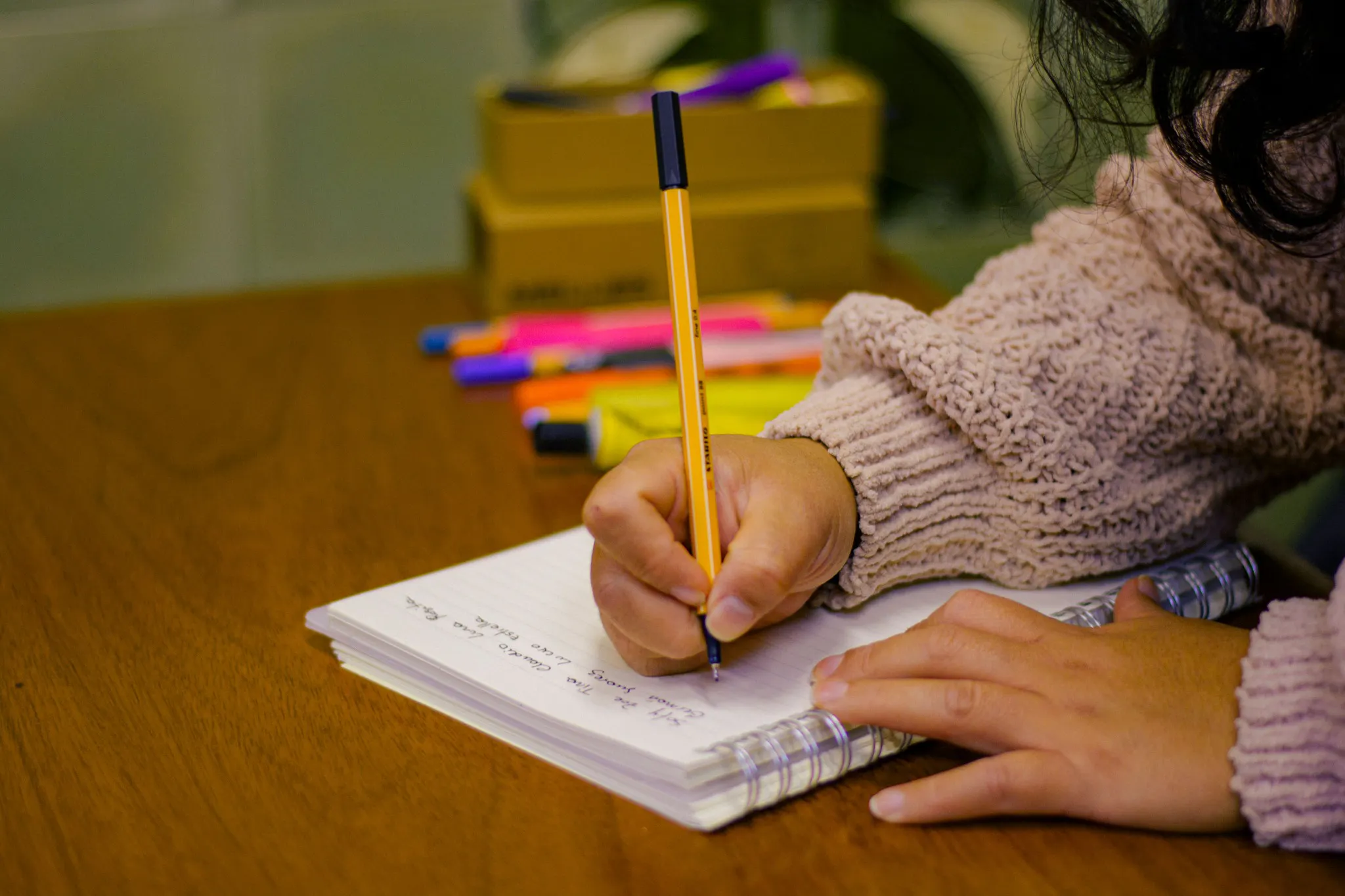 Person writing study notes in a spiral notebook beside colorful highlighters