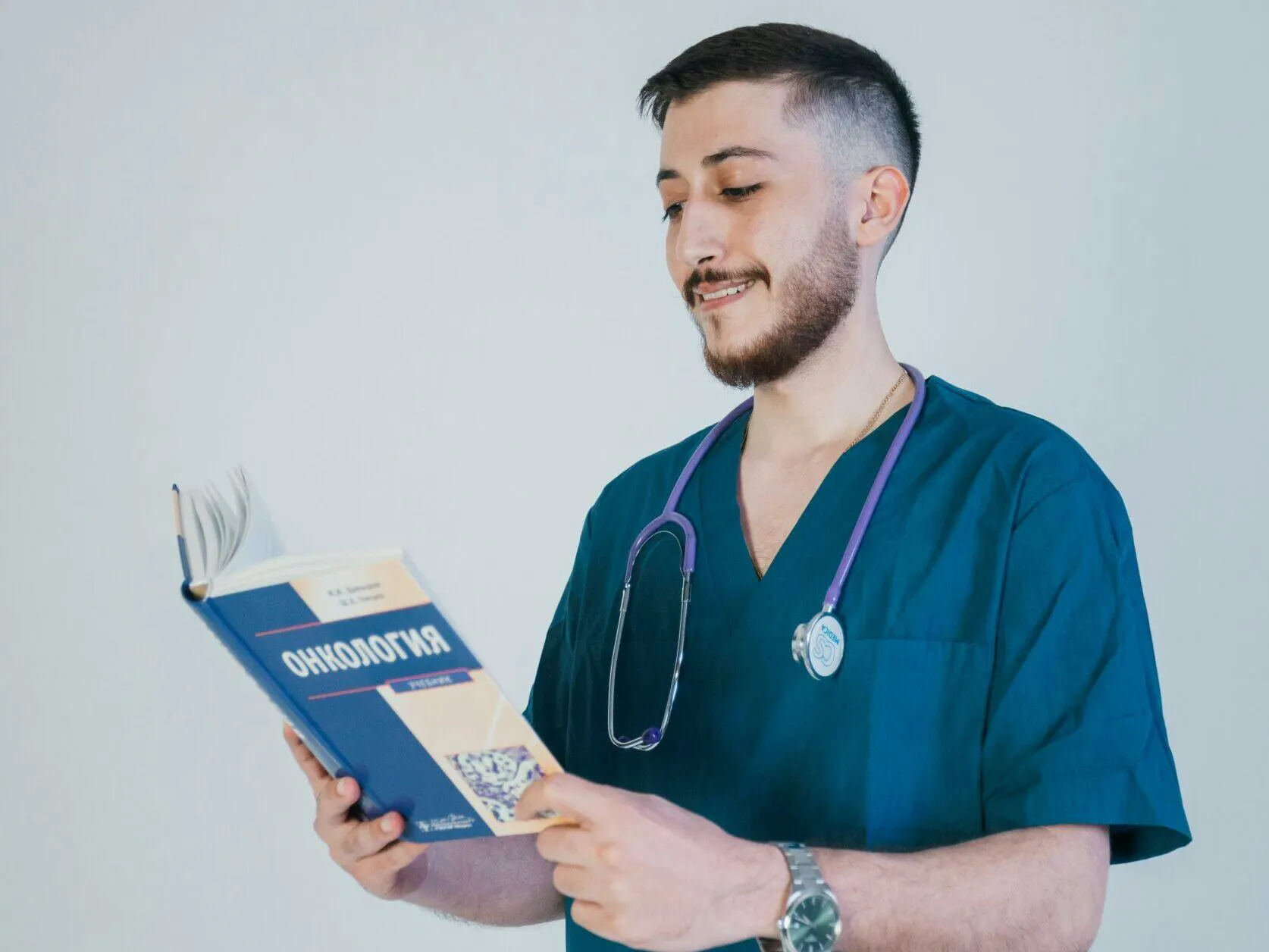 Nursing student in scrubs with a stethoscope reading a medical textbook