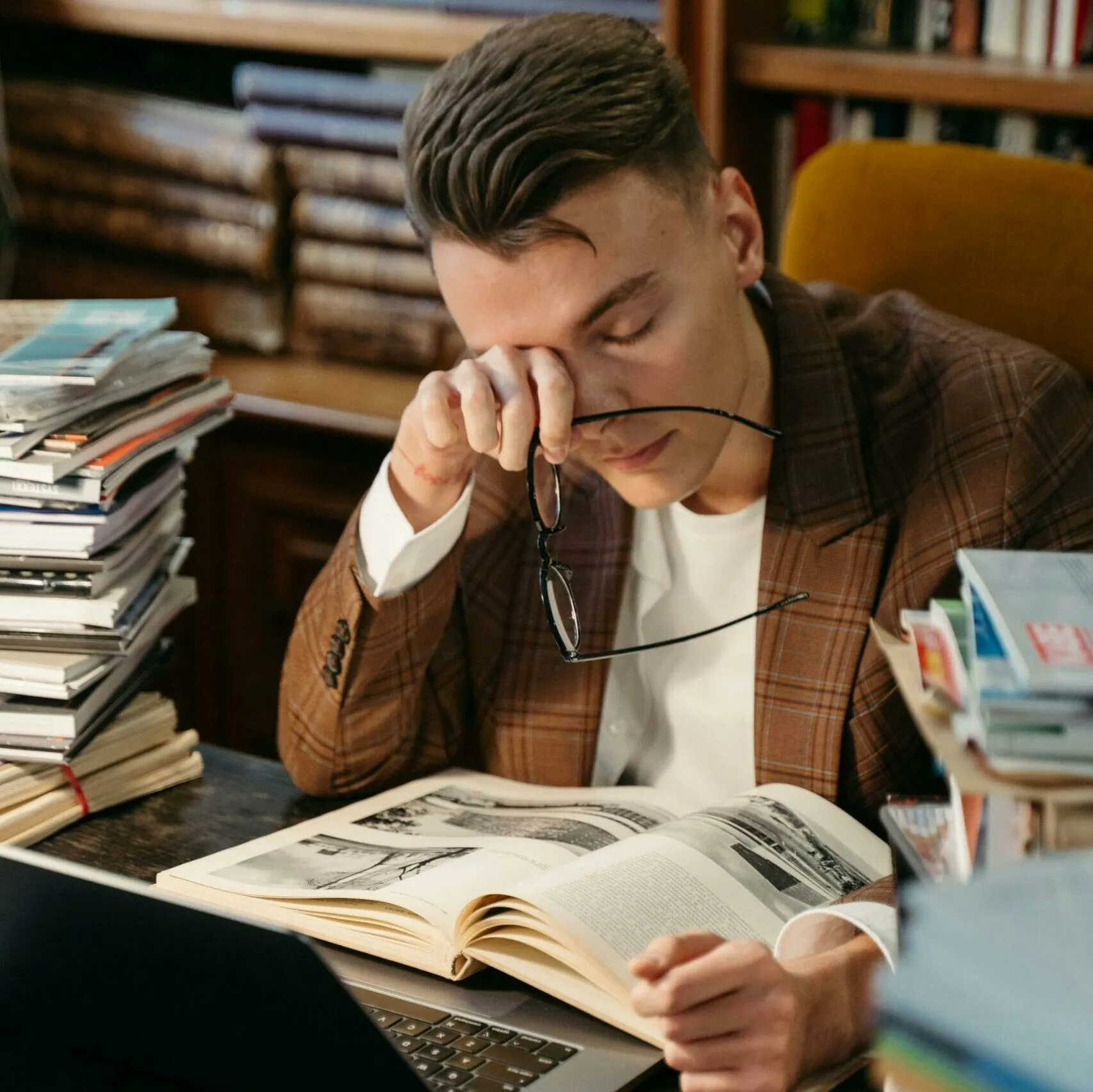 Tired student rubbing his eyes over a textbook and laptop while studying for the next gen NCLEX